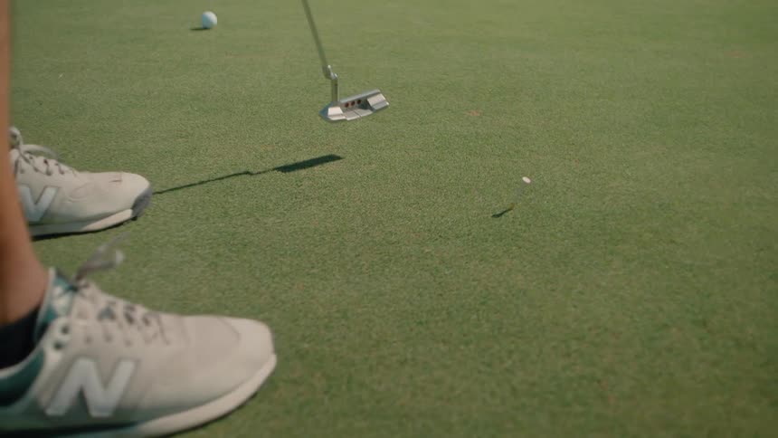 Man stands holding his golf club near the ball then hits the ball