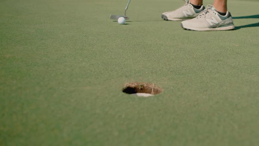 A golfer lines up a short putt on a vibrant green course the ball rolls smoothly across the grass and drops cleanly into the hole
