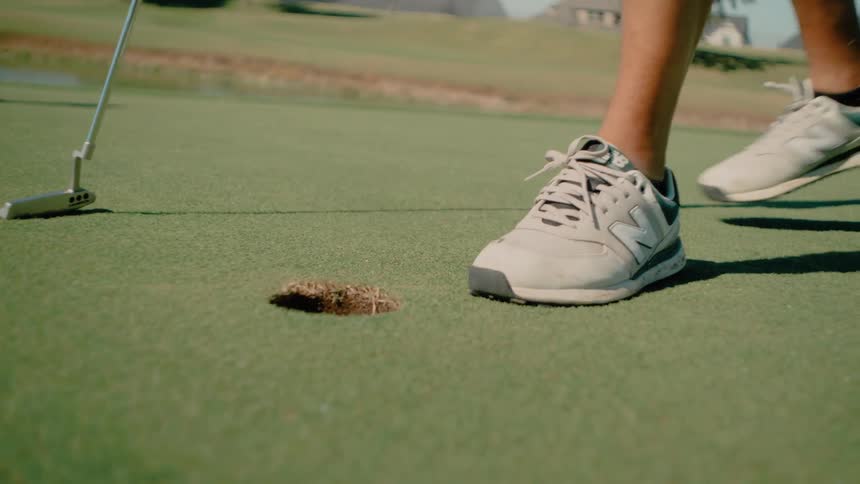 Person retrieving a golf ball from a target hole