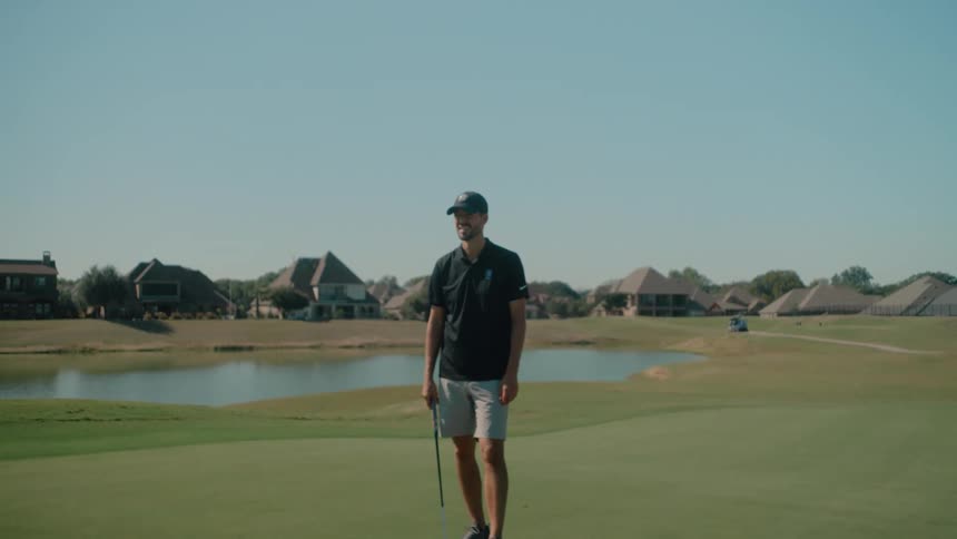 Young adult male golf player talking and gesturing before positioning next to a golf ball with a club in his hand outdoors during day time