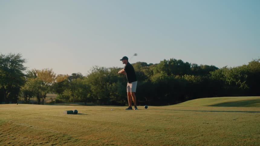 Man positions a golf ball on a green grass field and takes a swing