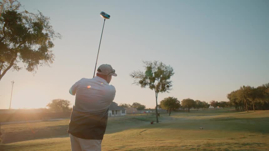 Man stands on the golf course and swings his golf club hard as he watches the ball fly