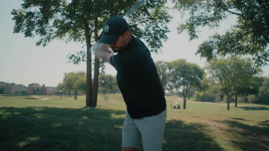 The man swings his golf club and watches the ball fly