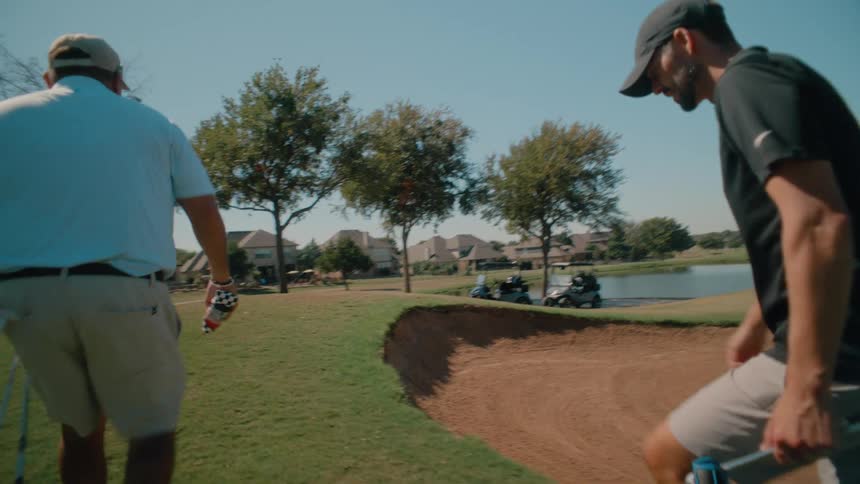 Two male adult golf players greeting and then walking together on the field carrying golf clubs outdoors during day time