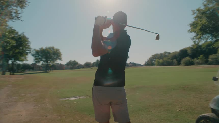 A golf player swings his club to hit the ball on the course at midday