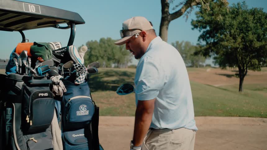 Man in cap picks up a golf club from a golf cart