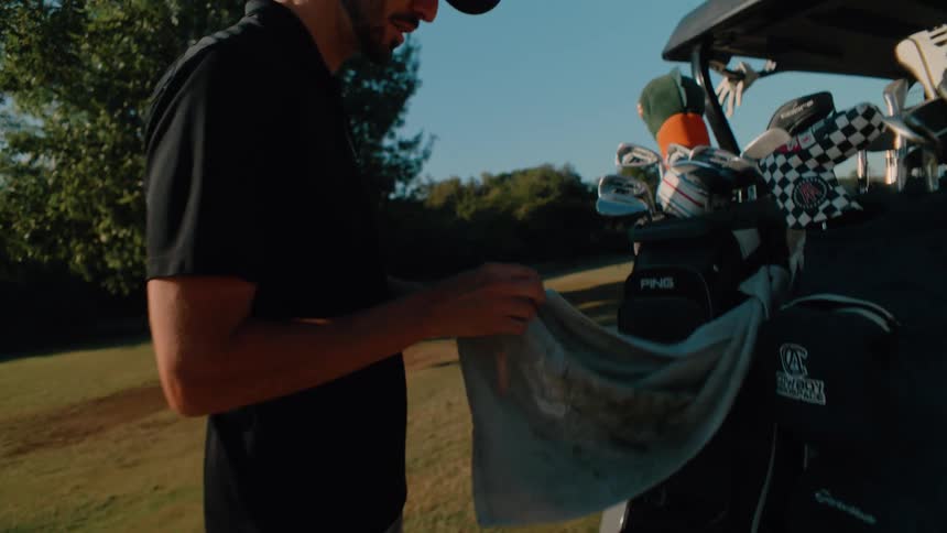Two men golfing outdoors and loading clubs into a golf cart