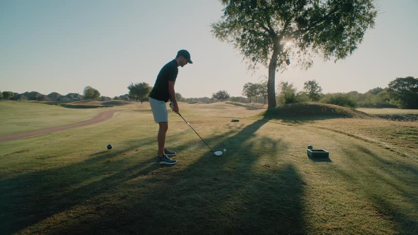 Man holds his golf club as he walks to balls on tees and hits them