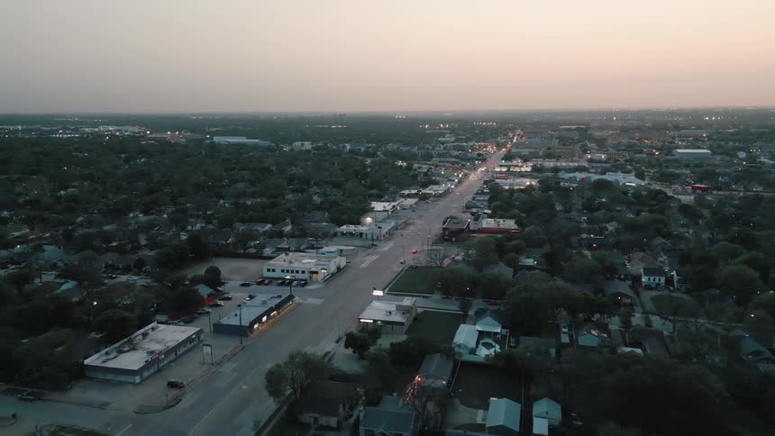 Aerial view shows a main avenue cutting through an urban neighborhood with light traffic at dusk