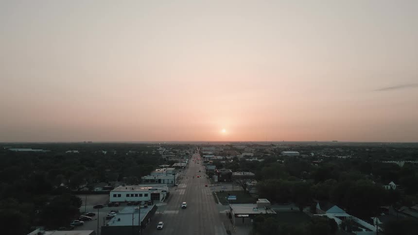 Urban avenue stretches straight under the sunset with buildings and trees surrounding it