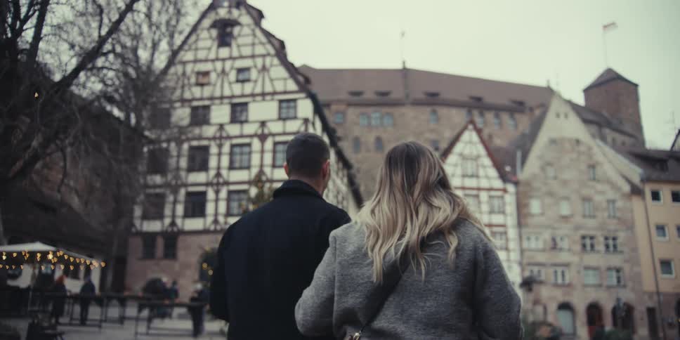 Man and woman walking together in front of an apartment building with other people on the street