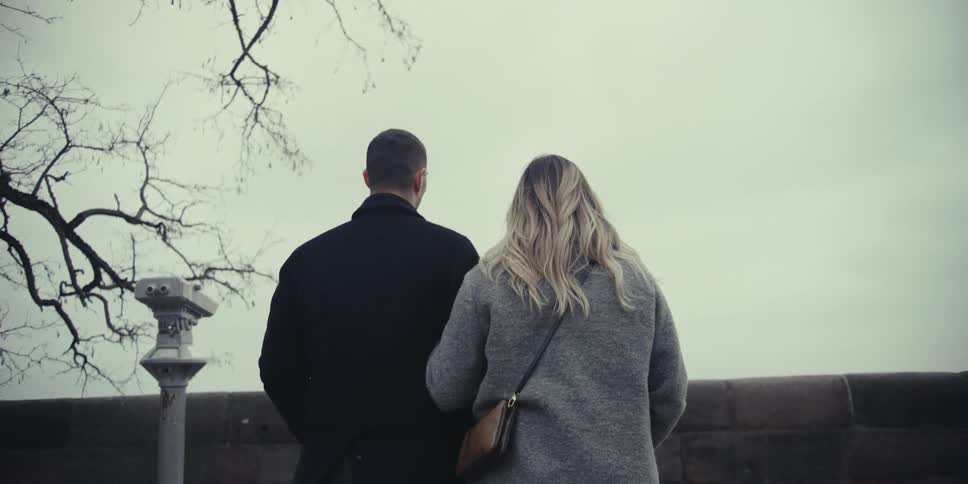Man and woman walking together near a bare tree to a railing overlooking the neighborhood below