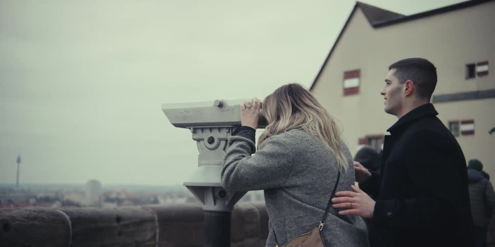 A man and woman take turns looking through a set of binoculars