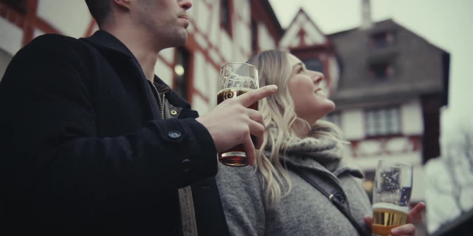 A happy couple enjoys drinks while sightseeing in a quaint european style town at dusk