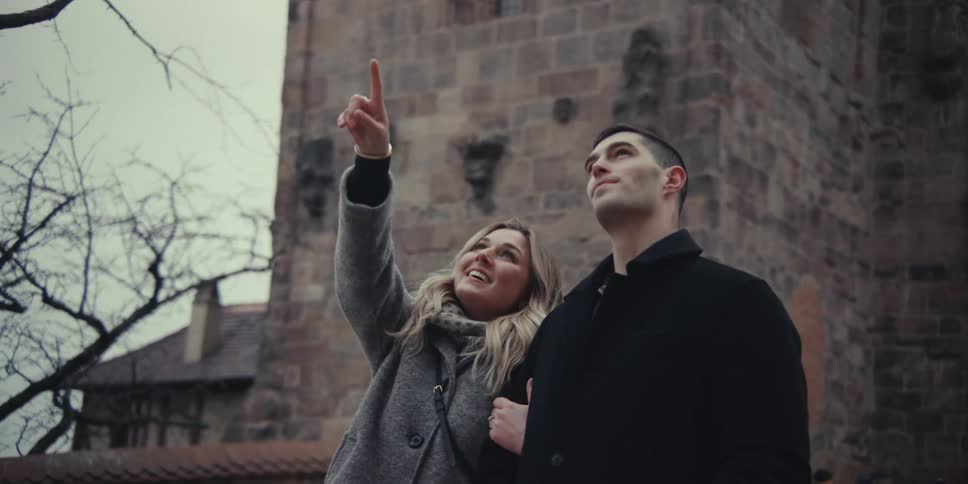 A smiling couple walks together outdoors exploring a historic stone estate