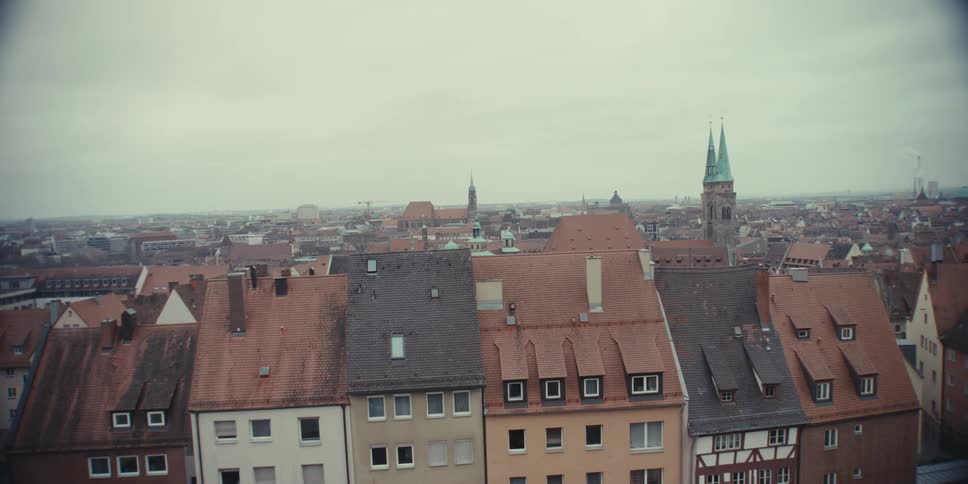A slow pan reveals the sprawling rooftops of an ancient european city stretching out towards the horizon under a soft overcast sky