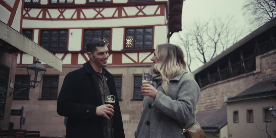 Couple walks along a historic street holding beer glasses