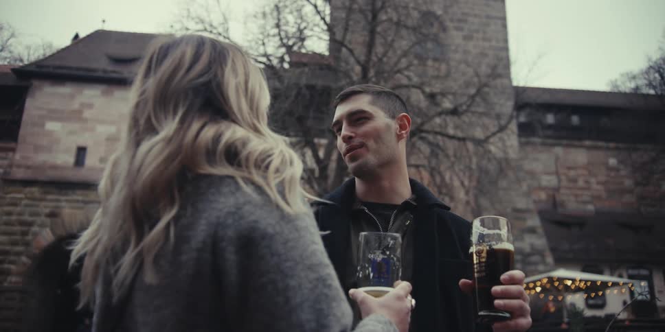 Couple talks in an outdoor urban setting while holding beer glasses