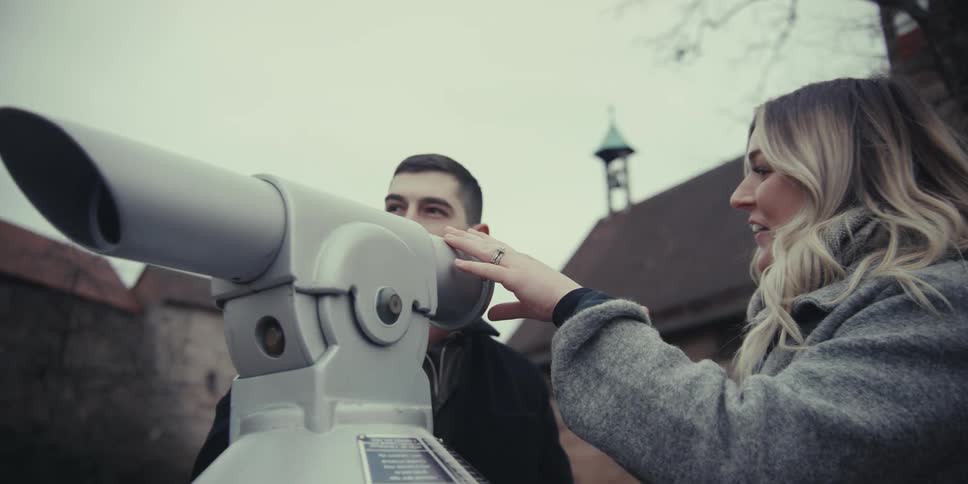 A young couple takes turns looking through a tourist telescope at a scenic historical site