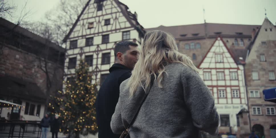A couple walks then stands outdoors smiling at each other while holding drinks sharing a relaxed moment in a historic town setting