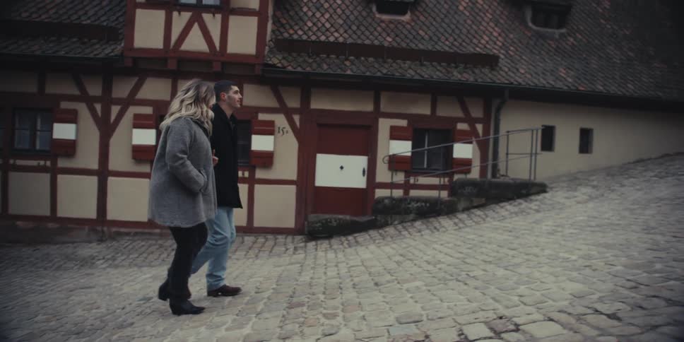 Couple walks along a cobblestone street in front of historic buildings