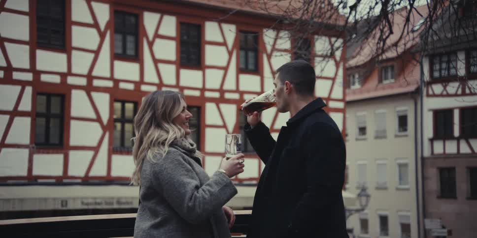 Man and woman standing among neighborhood buildings as they toast a drink