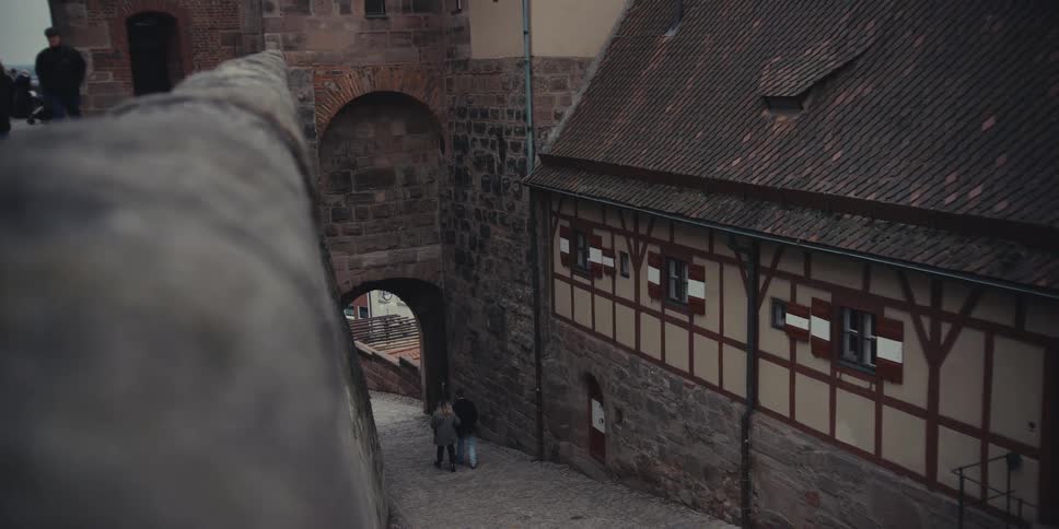A couple walks through an alley at midday holding hands as they step out toward the bright open street