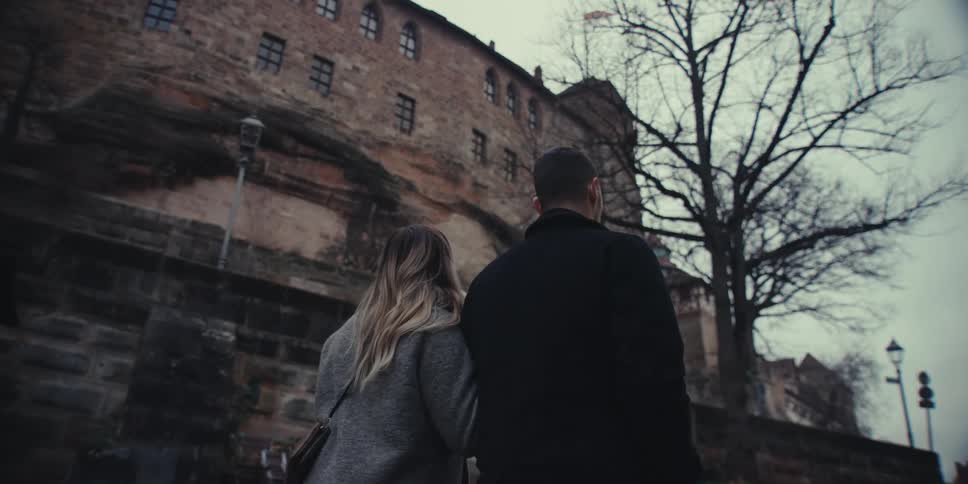 A couple walks together while admiring a historic stone building in an old european town