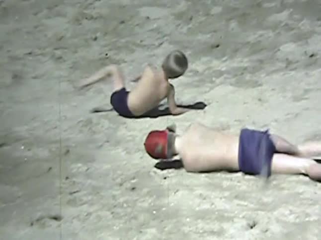 Children roll on a sandy dune under an open sky