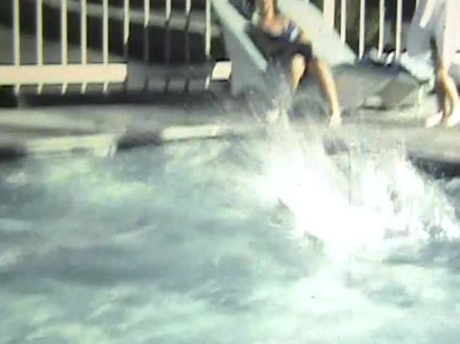 Woman sits and watches while one of her children jumps into the swimming pool