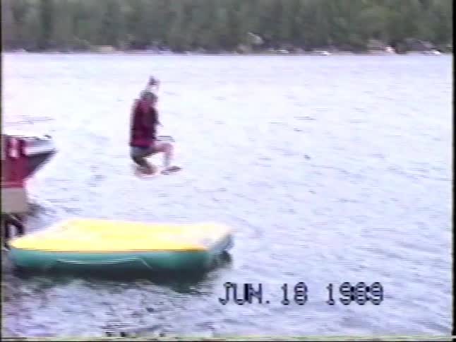 Teenager boy jumping from a pier into a river in front of other people standing there outdoors during day time