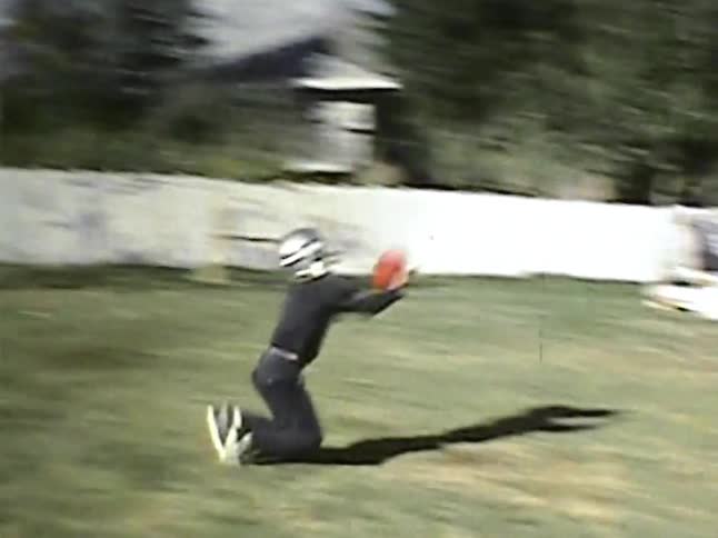 Two kids play with a football in a residential backyard on an autumn day