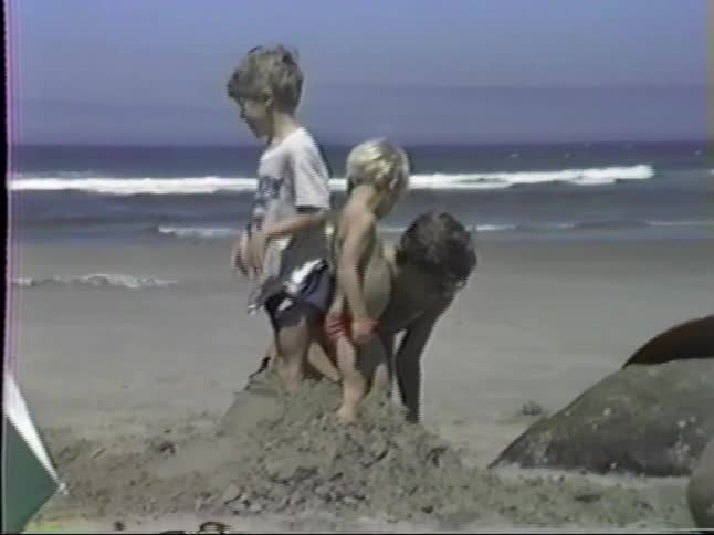 A mother and father play in the sand at a beach with their two boys