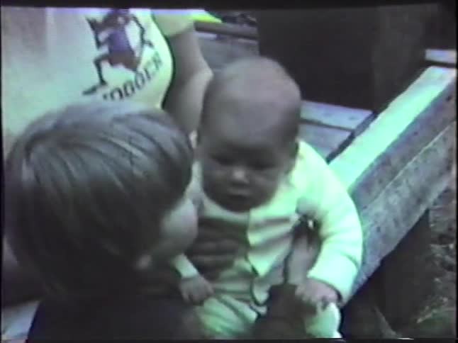 Young adult woman and toddler boy kissing and hugging a small baby that the woman is holding on her lap outdoors during day time