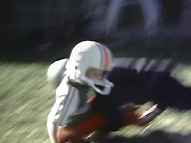 Two boys playing american football and falling on the grass field