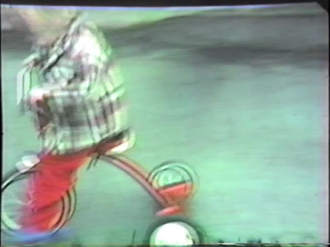 Father smiles while pedaling a bicycle with his toddler riding behind him and his older boy riding a tricycle