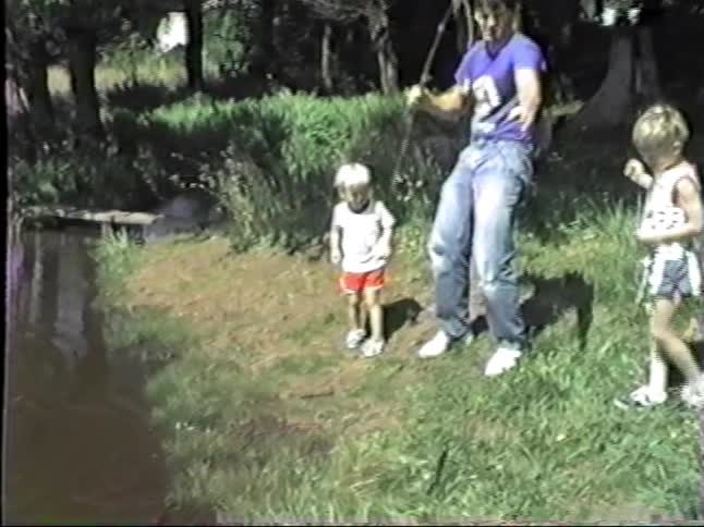 Young adult man at a riverbank catching a fish with a rod and two kids getting startled by the movement of the fish outdoors during day time
