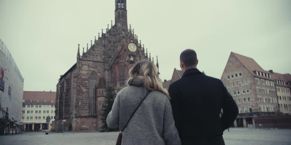 A couple strolls through a historic city square while admiring a large church building