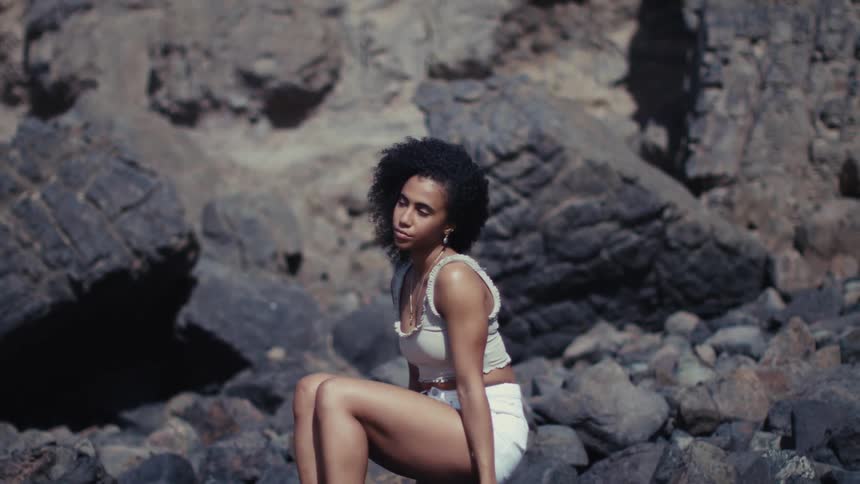 Woman sits on rocks in a coastal natural setting