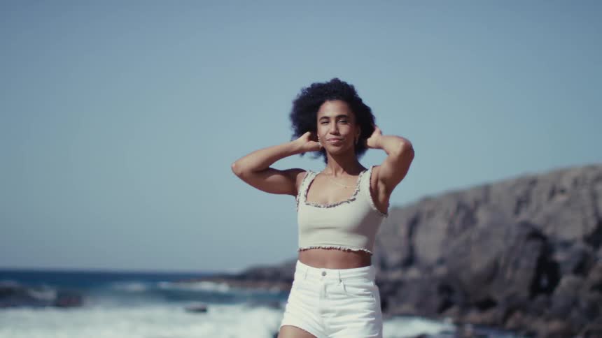 Woman standing on the beach smiles and fluffs her hair with her hands