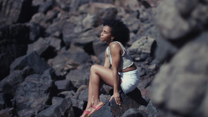 Young black adult woman sitting on a rock next to a cliff outdoors during day time