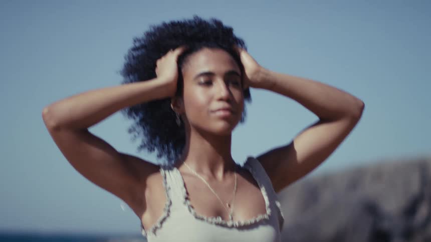 Young black adult woman posing in a beach next to the ocean outdoors during day time