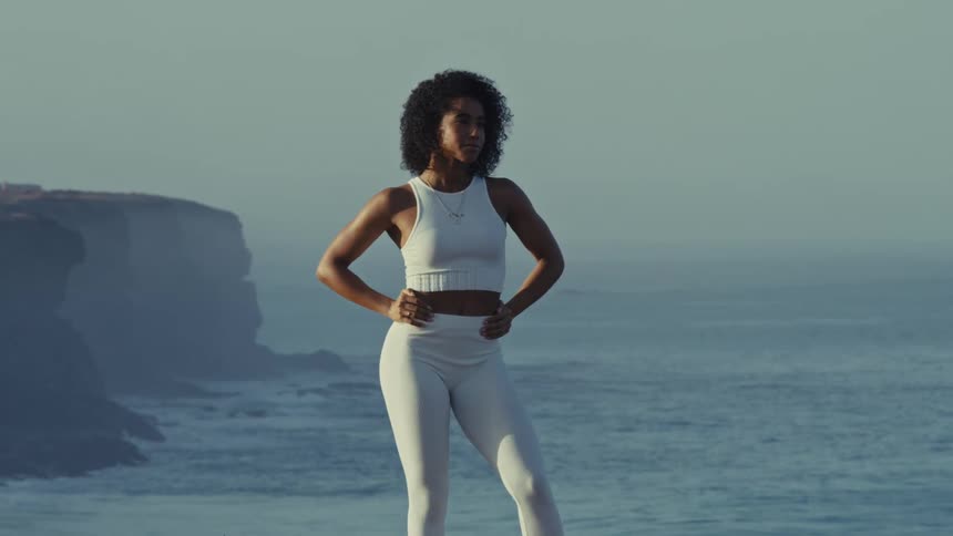 A fitness model poses confidently on a coastal cliff by the ocean during a photoshoot