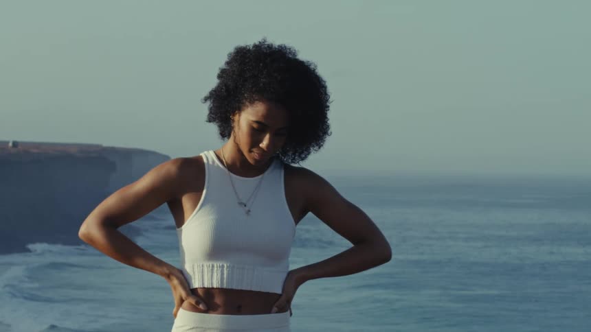 Bathed in sunlight a strong woman in athletic wear stands confidently on a cliffs edge gazing at the expansive ocean before her