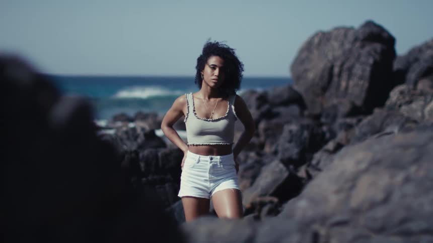 A young woman stands near a rock formation on an ocean shore