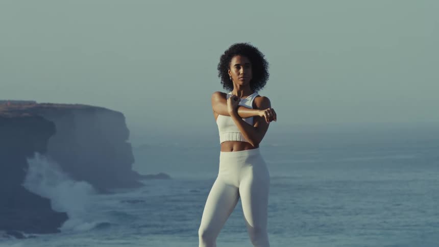 Woman standing along the coast doing stretching exercises