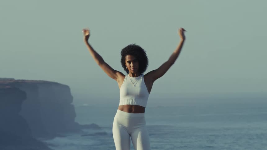 Woman stretches while performing yoga on a seaside cliff on a foggy day