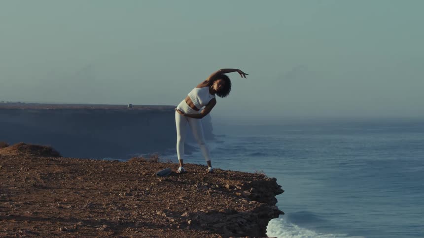 Woman standing near the edge of a seaside cliff on a foggy day stretches