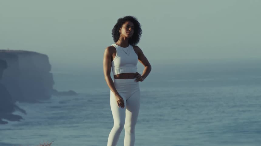 A young woman models white exercise clothing while standing near an ocean shore