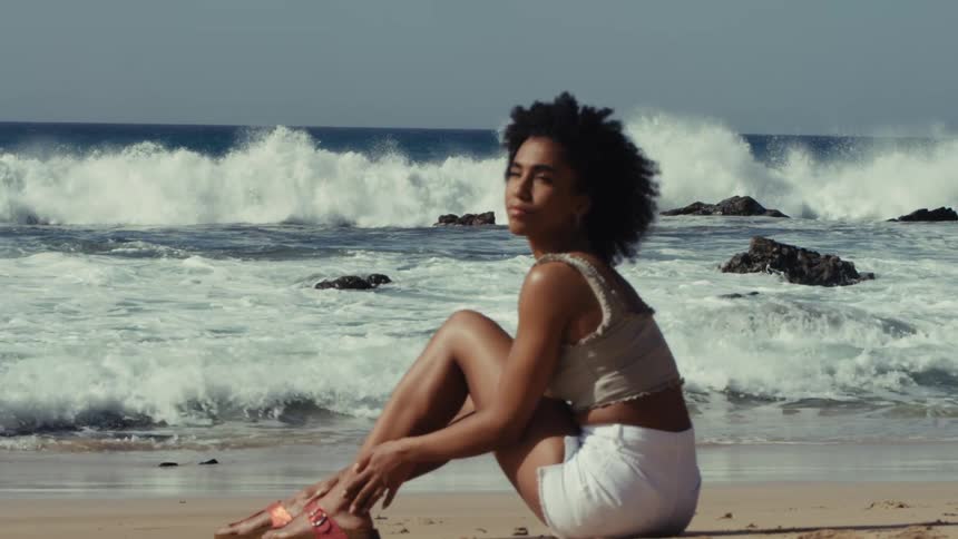 Woman sitting on the beach sand with waves breaking in the background